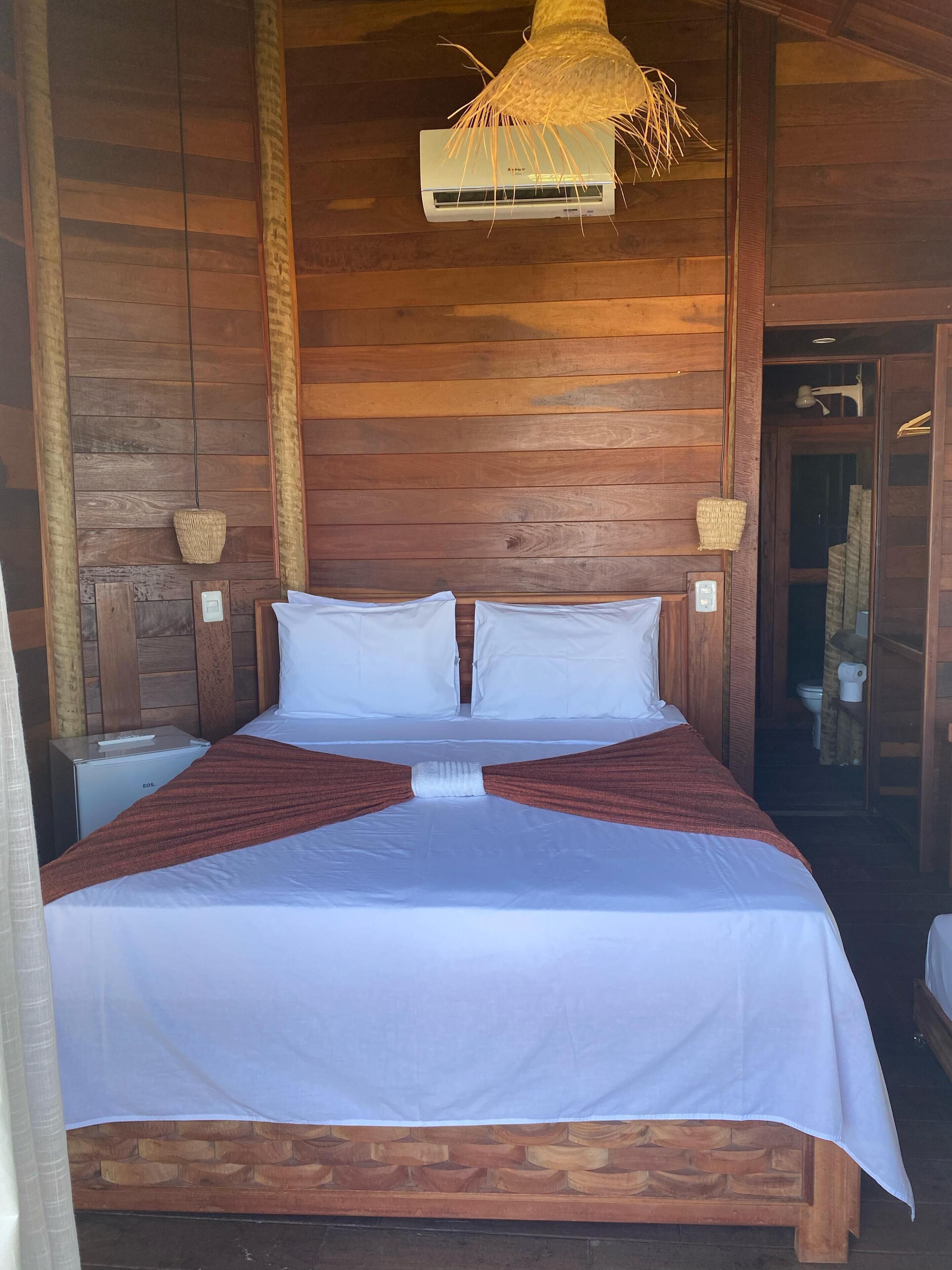 Una habitación tipo cabaña de madera con una cama, una mesita y una lámpara colgante.