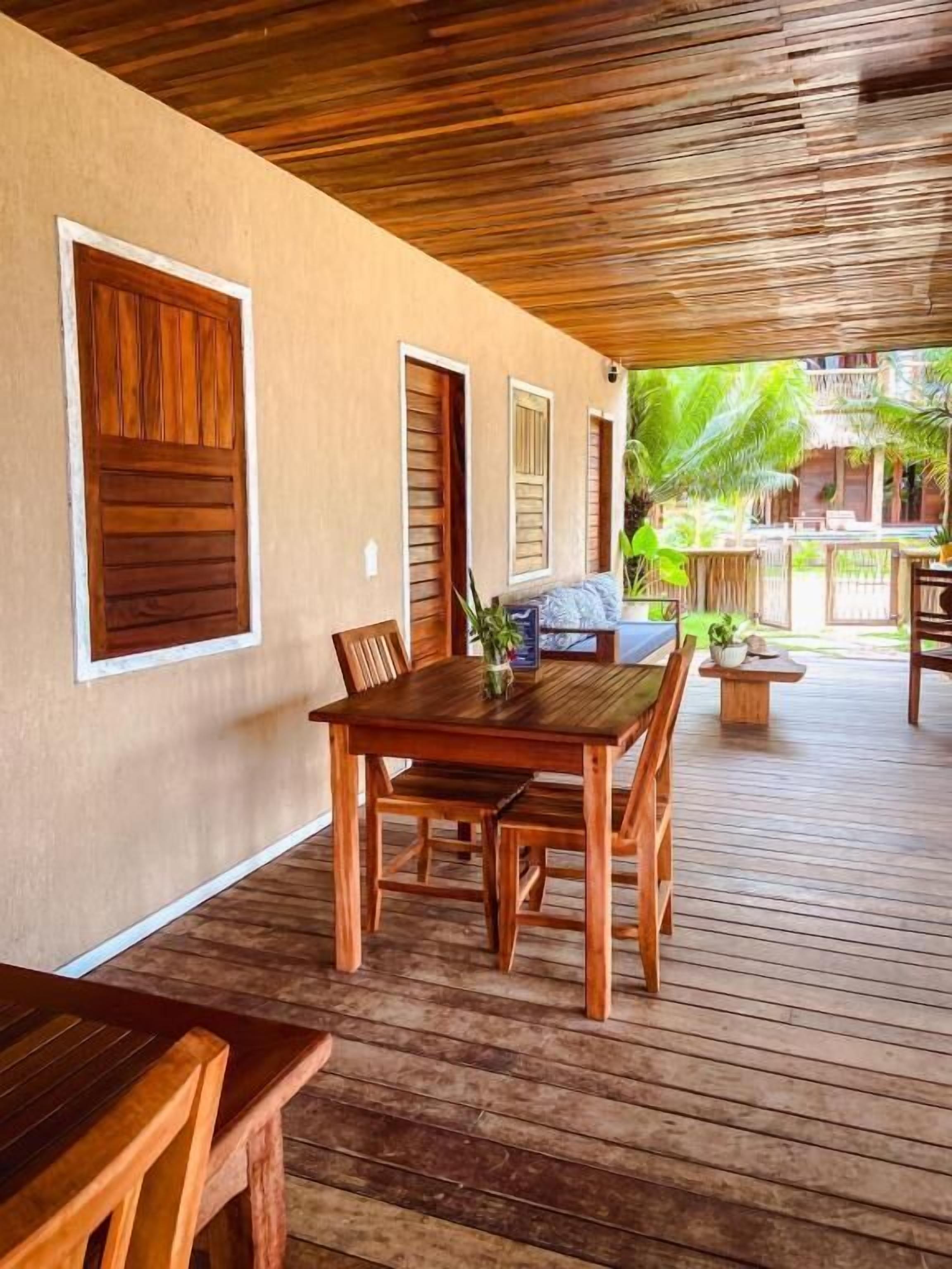 A wooden deck with a table and chairs, a covered area with a thatched roof, and a view of a tropical garden.