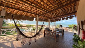A wooden deck with a hammock, wooden furniture, and a view of the ocean. - Caravelas Praia (Amontada)