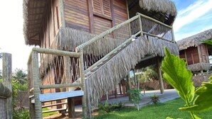 A traditional thatched-roof building with a wooden staircase leading to a balcony. - Caravelas Praia (Amontada)