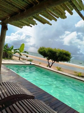 A wooden deck with a swimming pool, a beach view, and a small tree. - Caravelas Praia (Amontada)