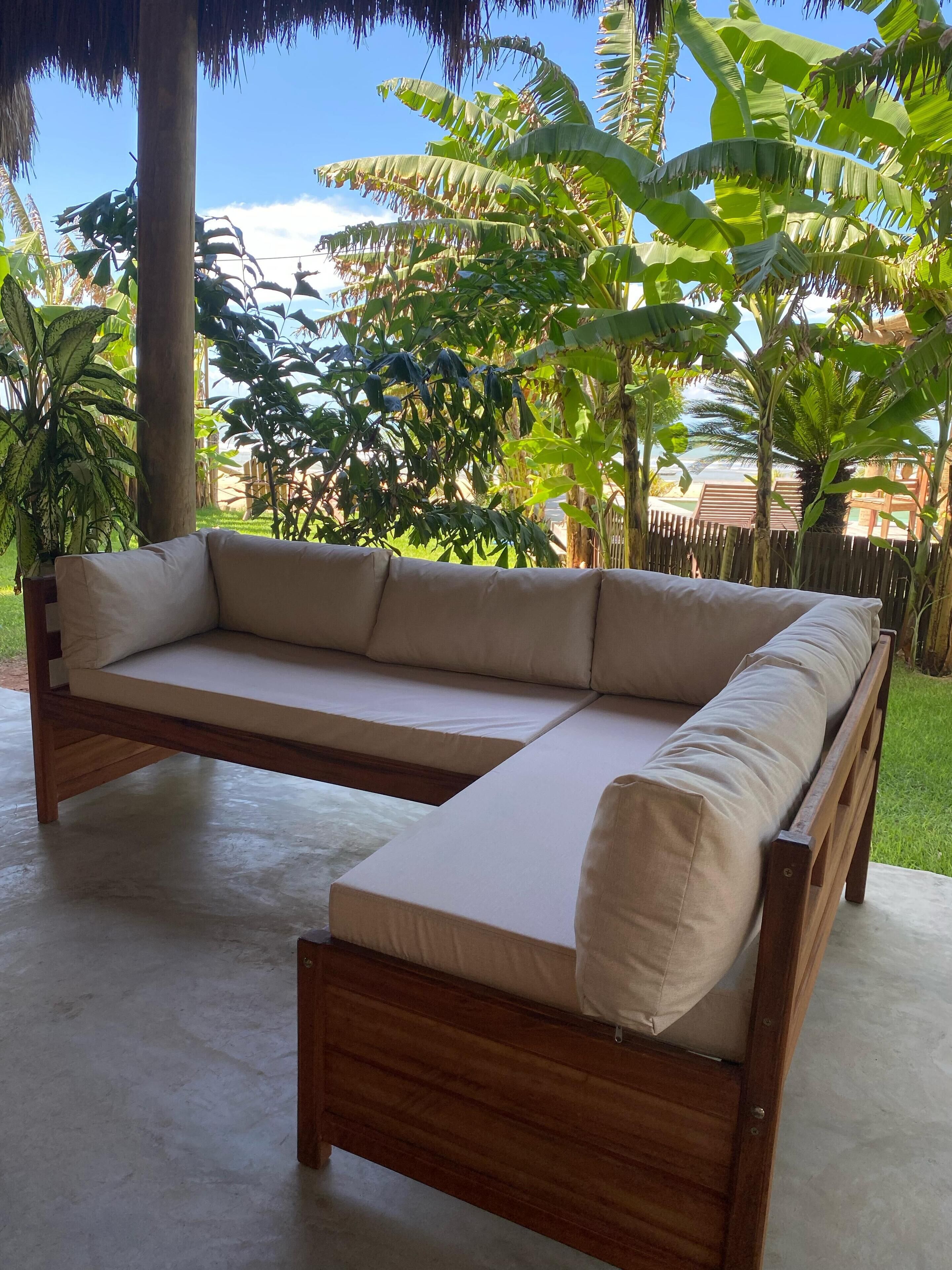 Ein modulares Sofa aus Holz mit beigefarbenen Kissen in einem überdachten Außenbereich.