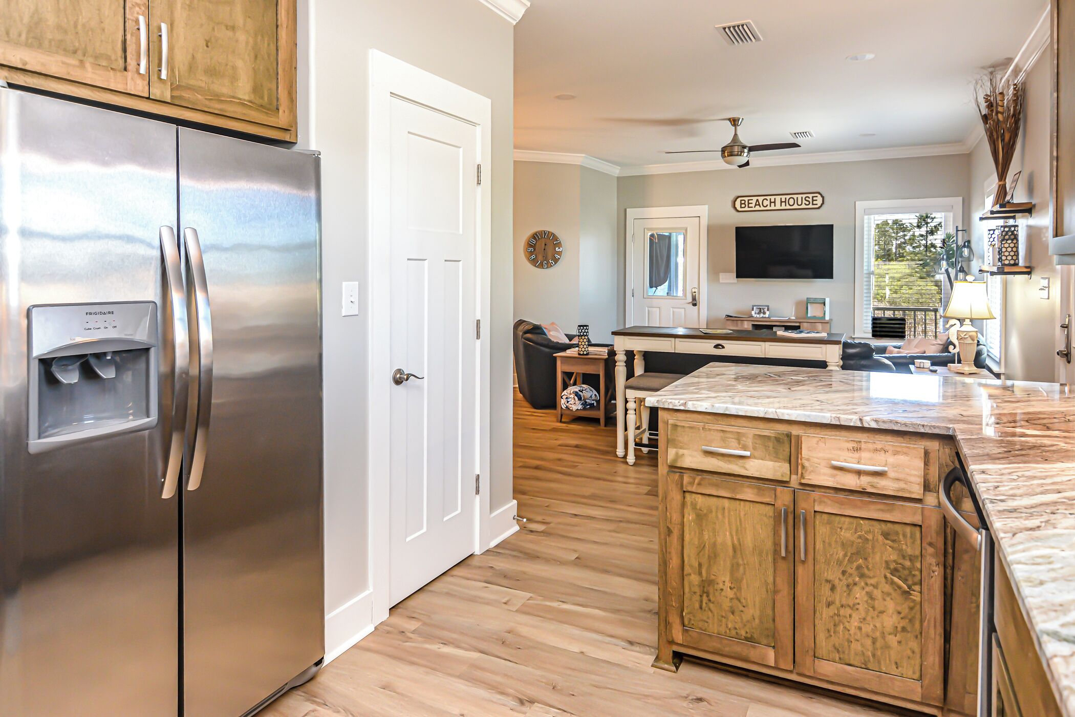 A kitchen with a stainless steel refrigerator, wooden cabinets, a marble countertop, and a ceiling fan.