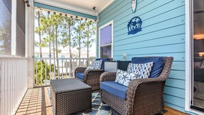 A covered porch with wicker furniture, a blue wall, and a view of trees.