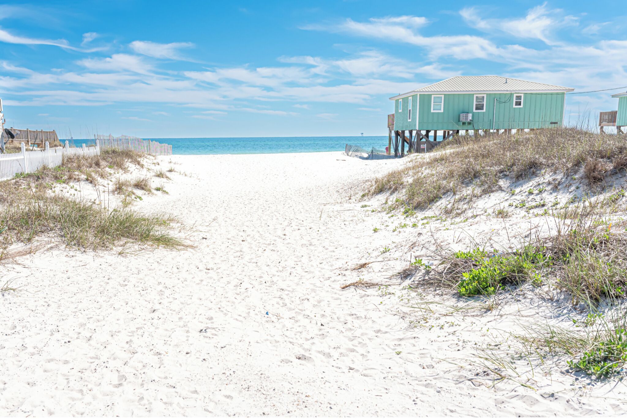 A beach path leading to a house on stilts with a view of the ocean.