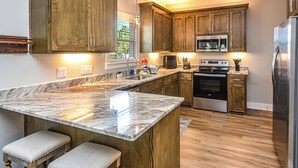 A kitchen with wooden cabinets, a marble countertop, a built-in oven, and a stainless steel refrigerator.