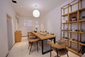 A modern dining area with a long table, chairs, a projector screen, and a bookshelf. - Wenzhou Taiyi Smart Hotel (Jingshan Park General Bridge Branch) (Wenzhou)