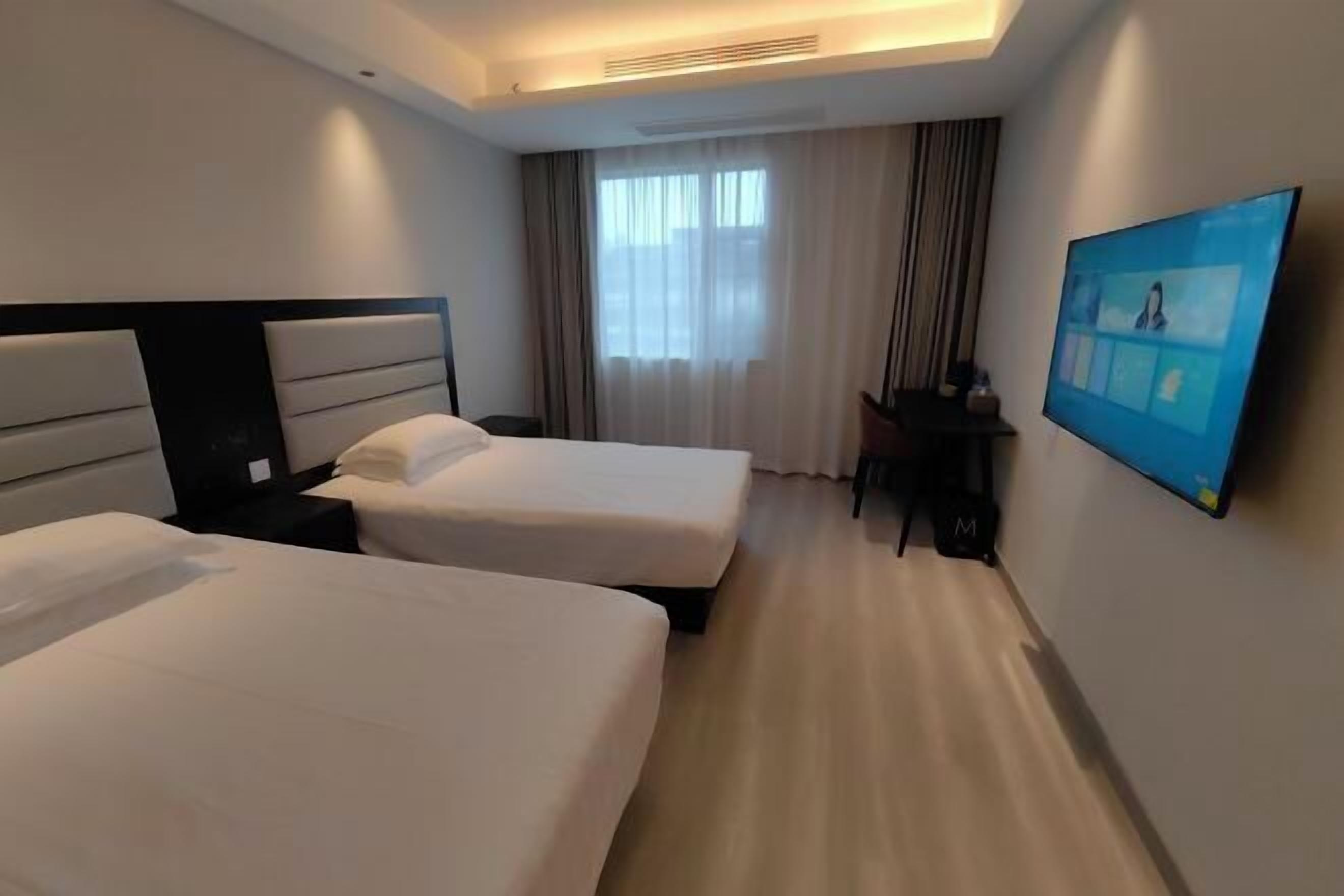 Une chambre d’hôtel avec deux lits, un bureau, une chaise, une télévision et une fenêtre avec des rideaux.