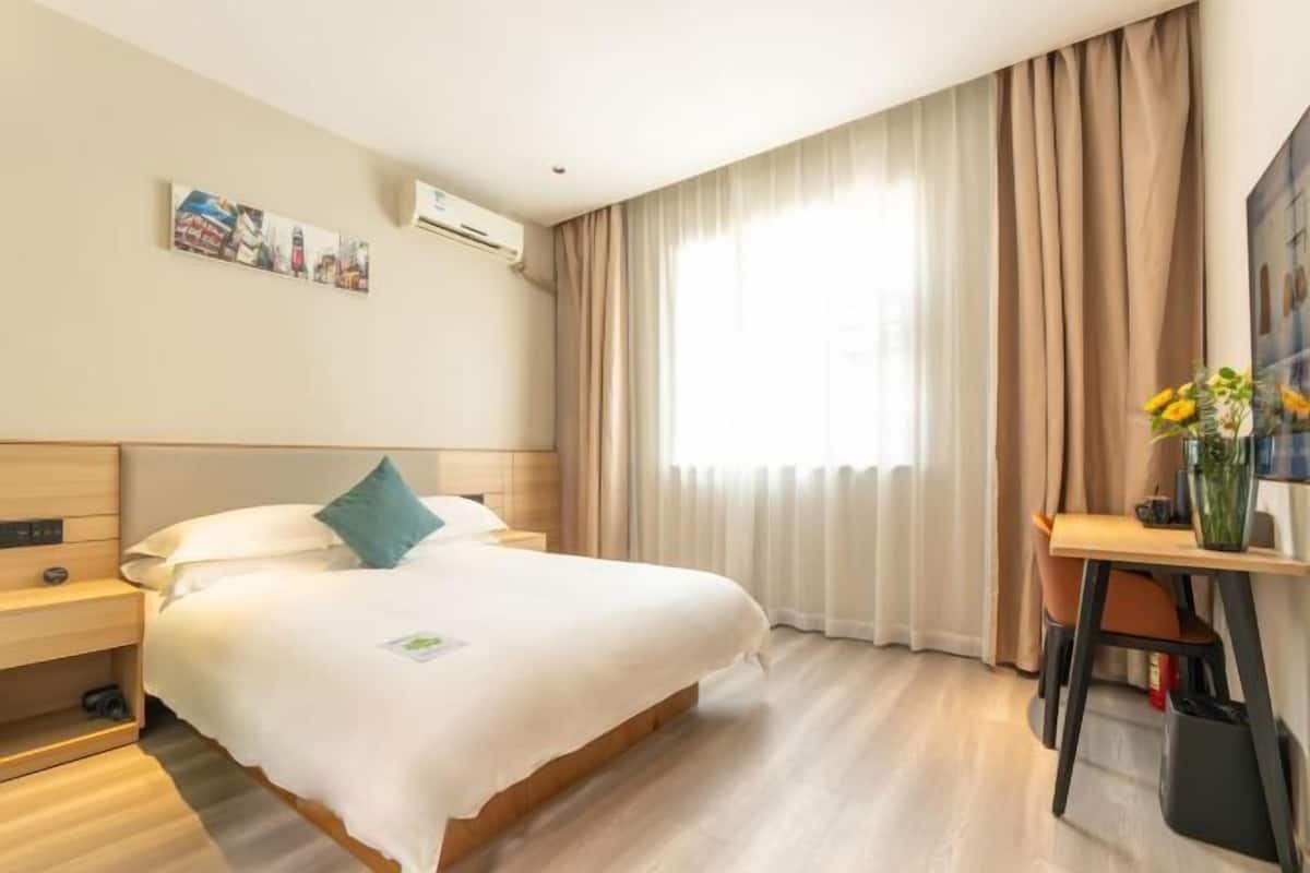Habitación de hotel con cama, escritorio, silla, ventana con cortinas y aire acondicionado instalado en la pared.