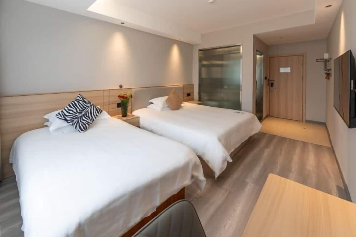 Habitación de hotel con dos camas, cabecero de madera, una mesita y una puerta que da al baño.