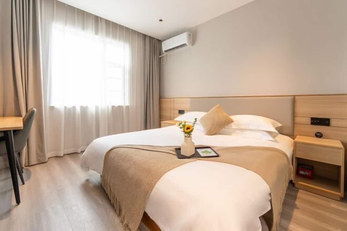 Una habitación de hotel con cama, mesita de noche, silla y equipo de aire acondicionado.