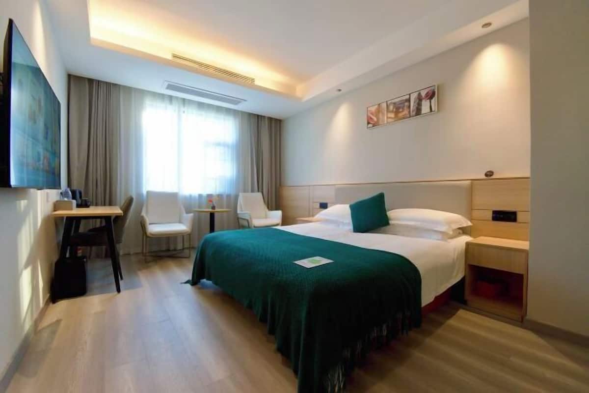 Habitación de hotel con cama, escritorio, silla, televisor y ventana con cortinas.