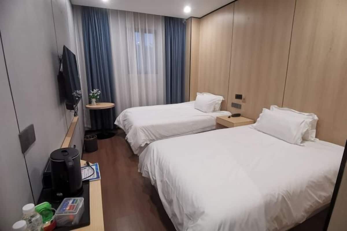 Habitación de hotel con dos camas, una mesita, un televisor y una ventana con cortinas.