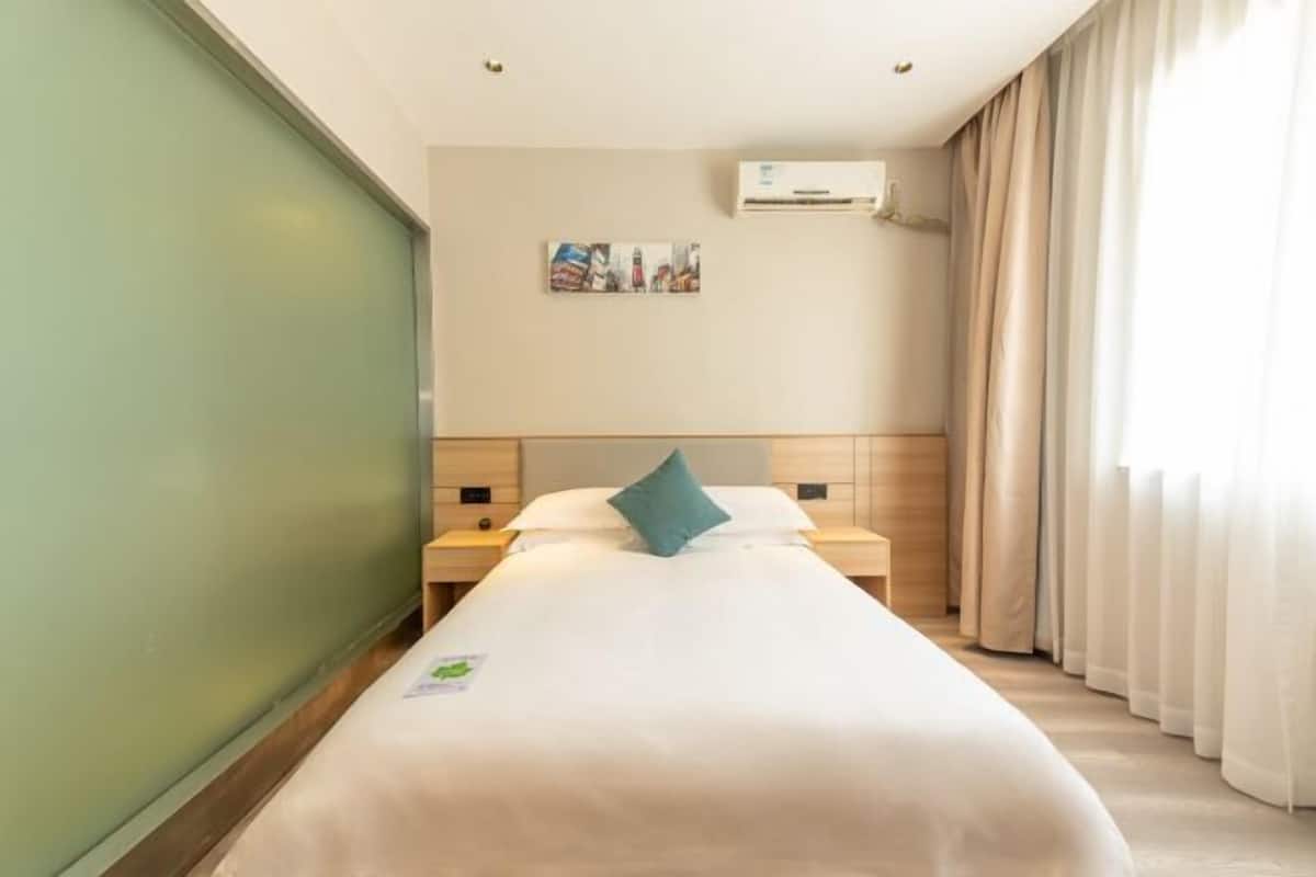 Una habitación de hotel con una cama, una mesita de noche, un equipo de aire acondicionado y una ventana con cortinas.