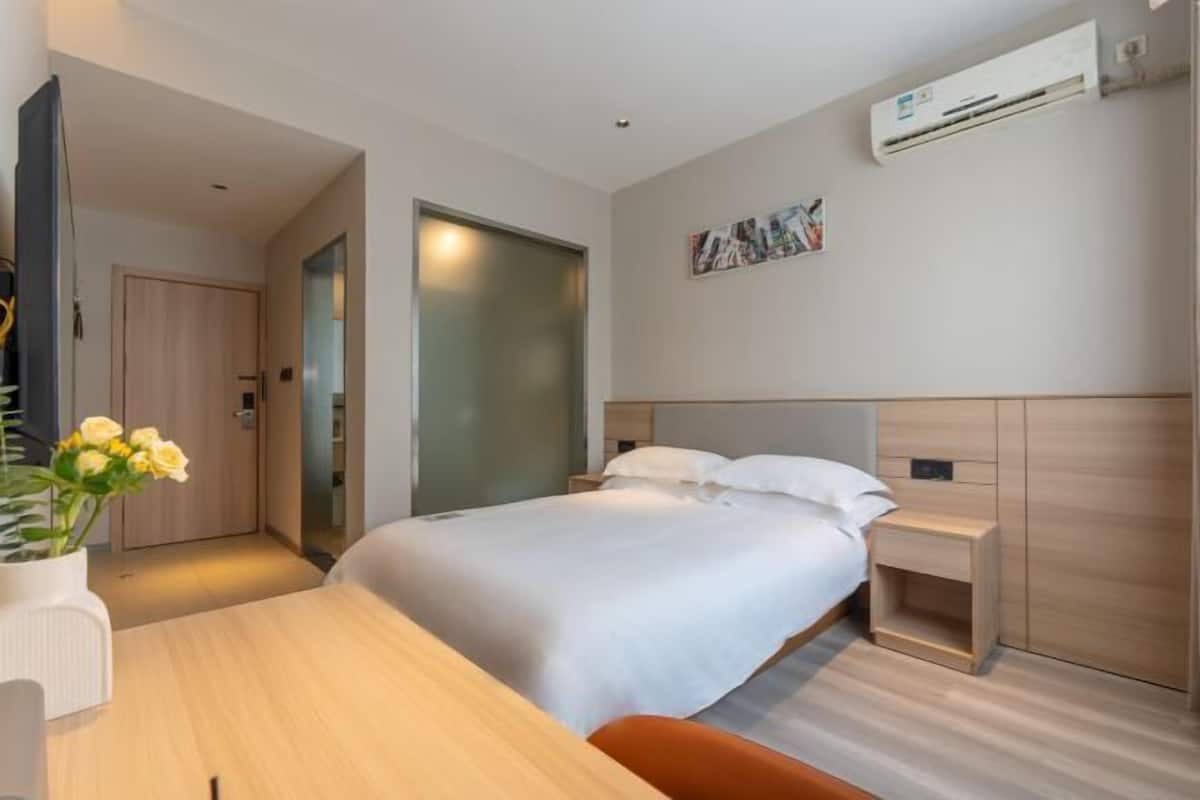 Una habitación de hotel moderna con cama, mesita de noche y un pequeño escritorio con silla.