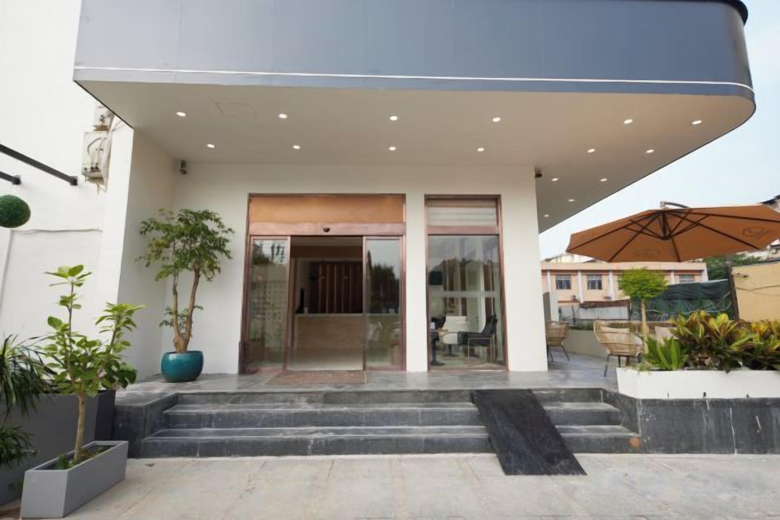 Una entrada de edificio moderna con techo plano, puertas de cristal y un pequeño espacio exterior con plantas.