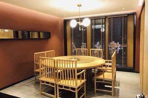 Uma área de refeições com uma mesa redonda e cadeiras, um lustre e uma porta de vidro deslizante que dá para uma varanda.