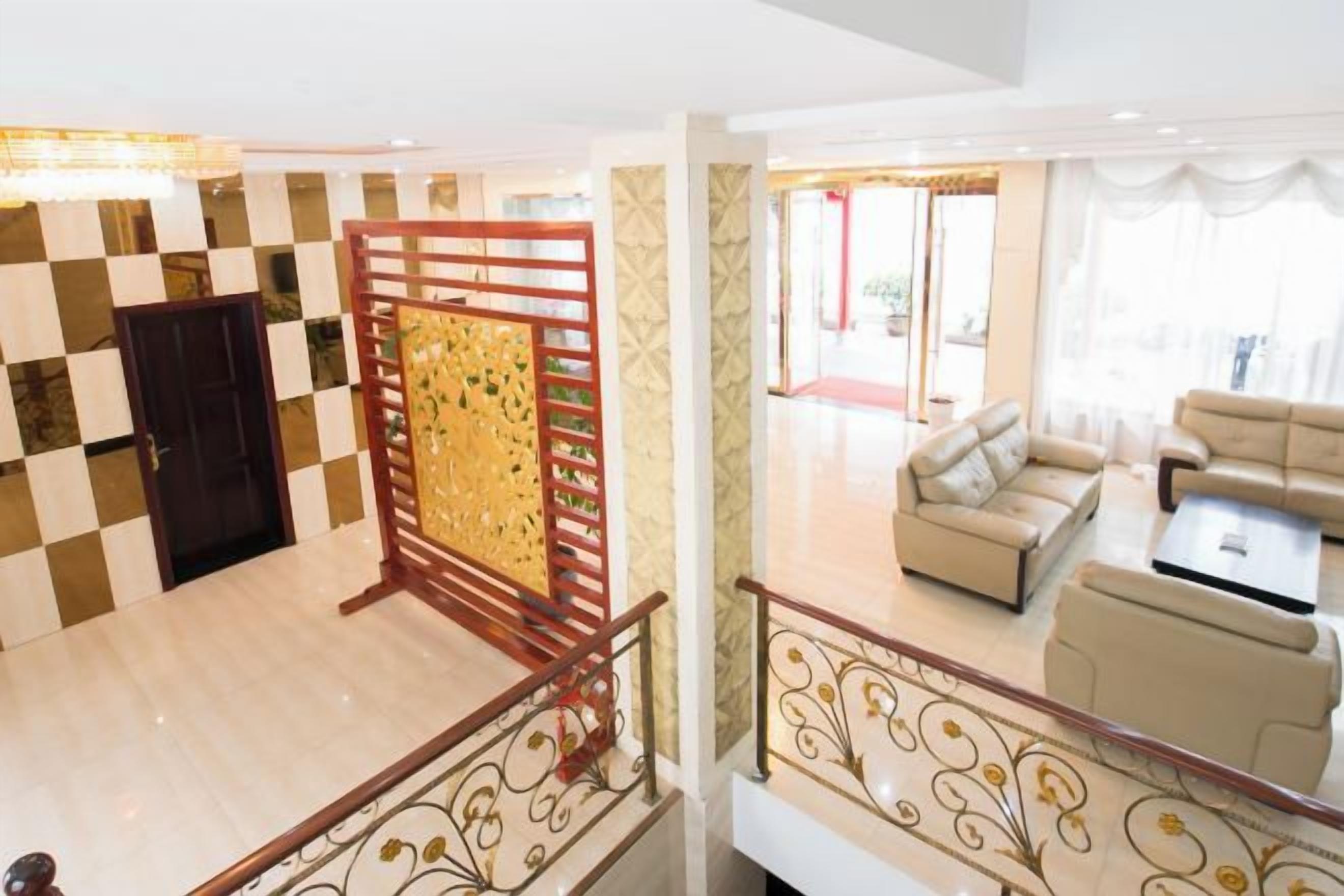A hotel lobby with a checkered floor, a wooden partition, a staircase with a railing, and a seating area with sofas and a coffee table.