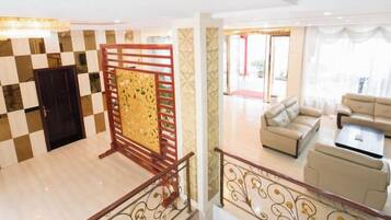 A hotel lobby with a checkered floor, a wooden partition, a staircase with a railing, and a seating area with sofas and a coffee table.