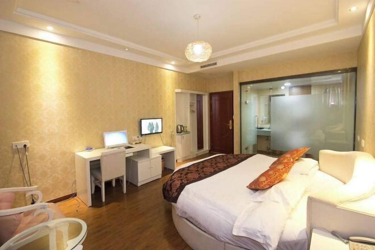 Une chambre d’hôtel équipée d’un lit, d’un bureau, d’une chaise, d’une télévision et d’une salle de bain avec une porte en verre.