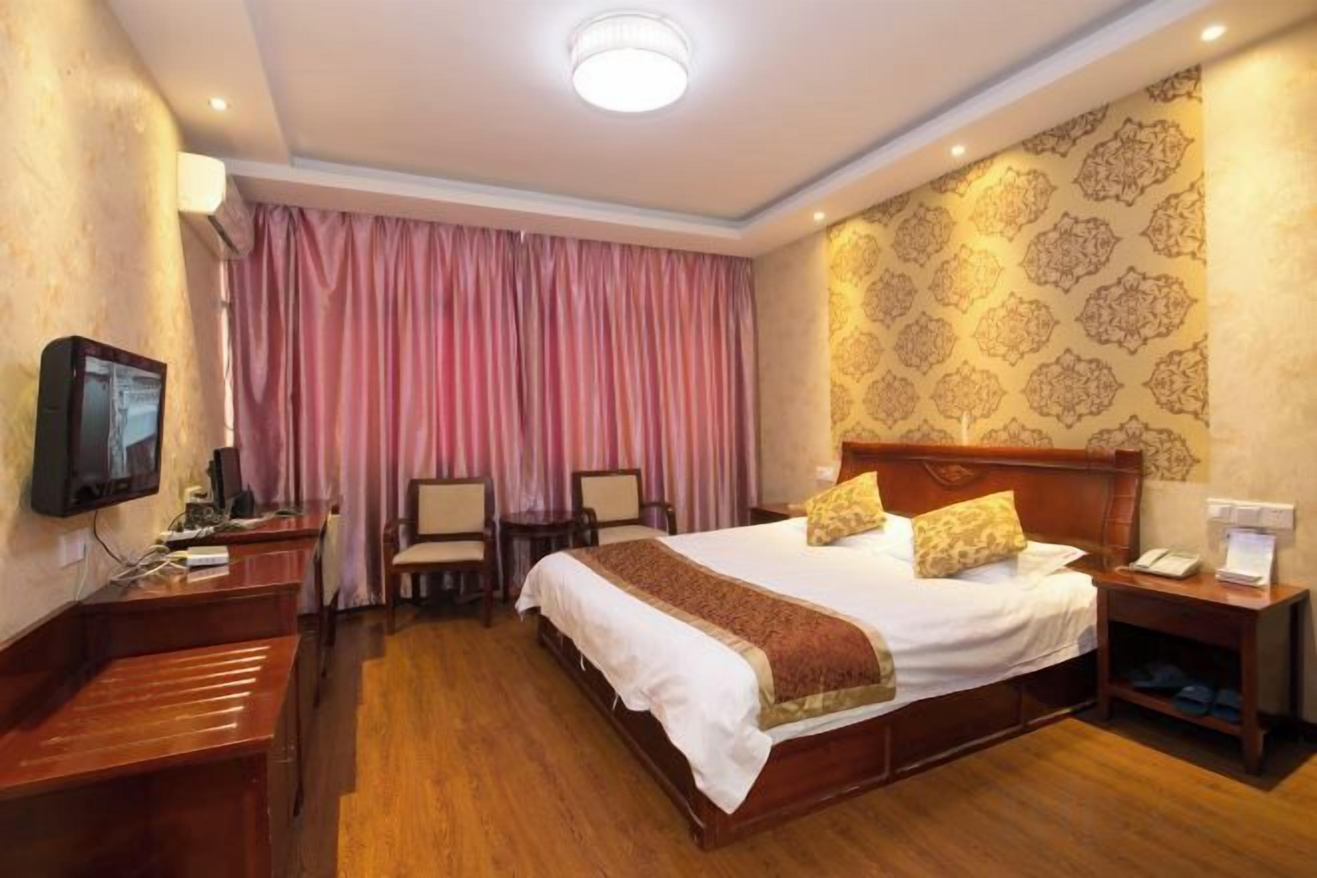 A hotel room with a large bed, bedside tables, a desk, a television, and a curtain.
