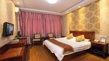 A hotel room with a large bed, bedside tables, a desk, a television, and a curtain.