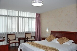 Una habitación de hotel con una cama grande, dos sillas, un escritorio y una ventana con cortinas translúcidas.
