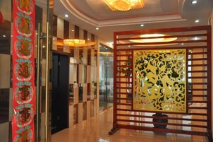 Un hall de hotel con una recepción, una pared decorativa con diseños intrincados y una lámpara de techo moderna.