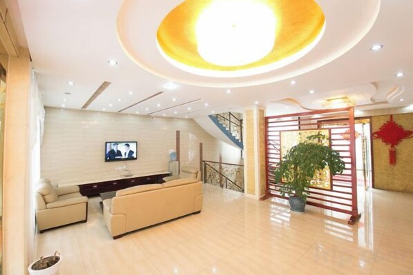 A spacious living area with a sofa set, a flat-screen TV mounted on the wall, a staircase, and a potted plant.