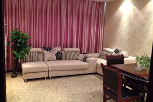 Uma sala de estar com um sofá bege, uma mesa de jantar e um vaso de planta.
