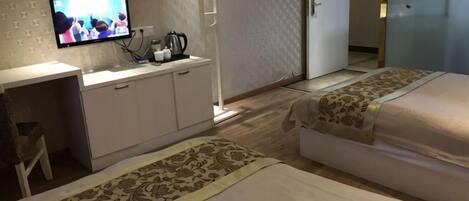 Une chambre d’hôtel avec un téléviseur posé sur un meuble, un bureau avec une chaise, deux lits recouverts de couvre-lits à motifs et un tapis à motifs.