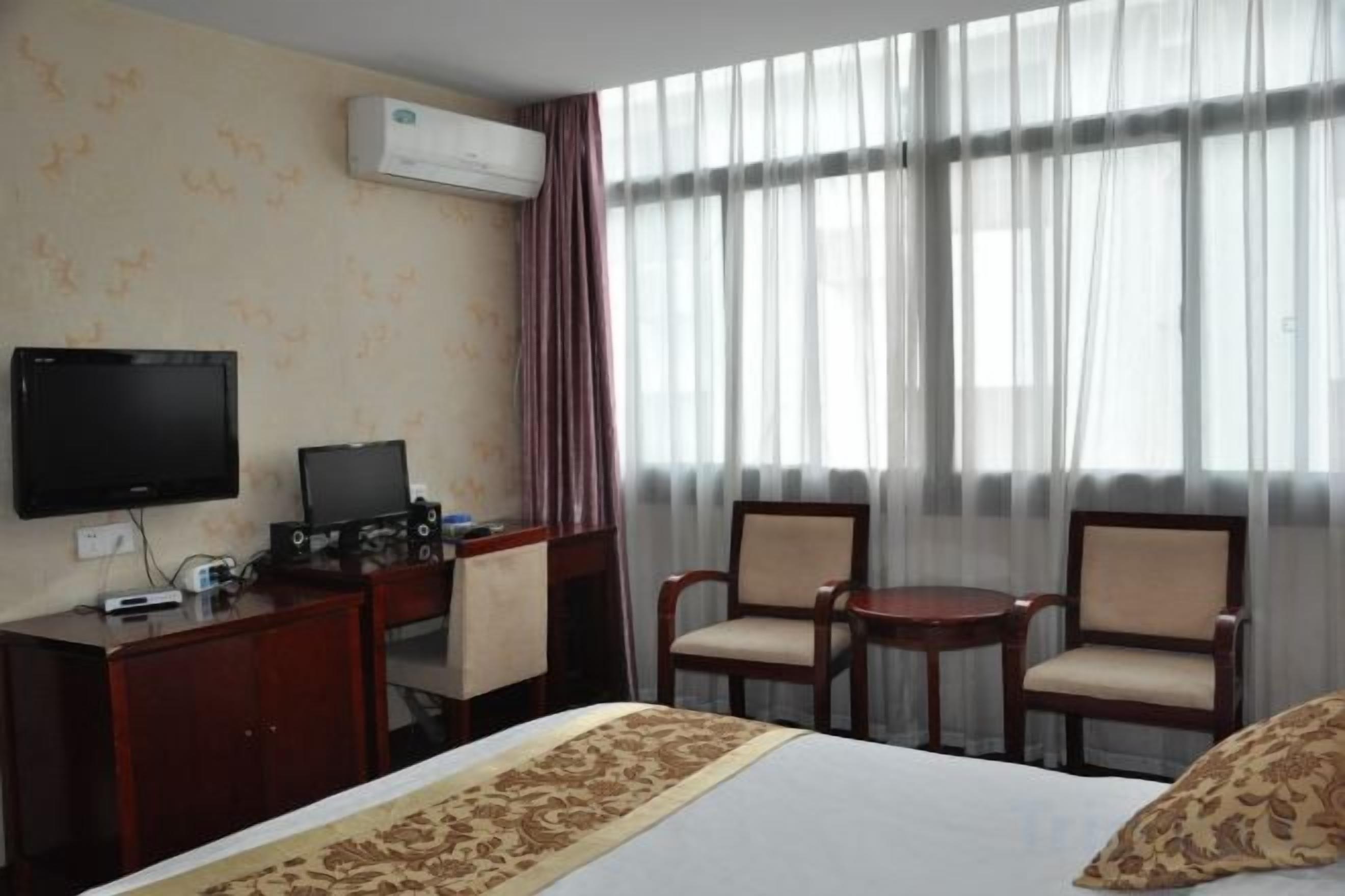 A hotel room with a bed, a desk with a computer, two chairs, and a television.