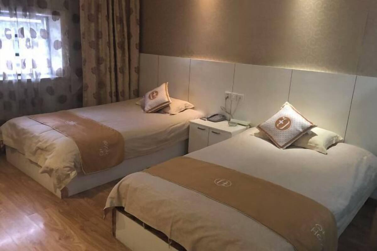 Deux lits jumeaux avec des têtes de lit assorties, une table de chevet avec une lampe et une fenêtre avec des rideaux.