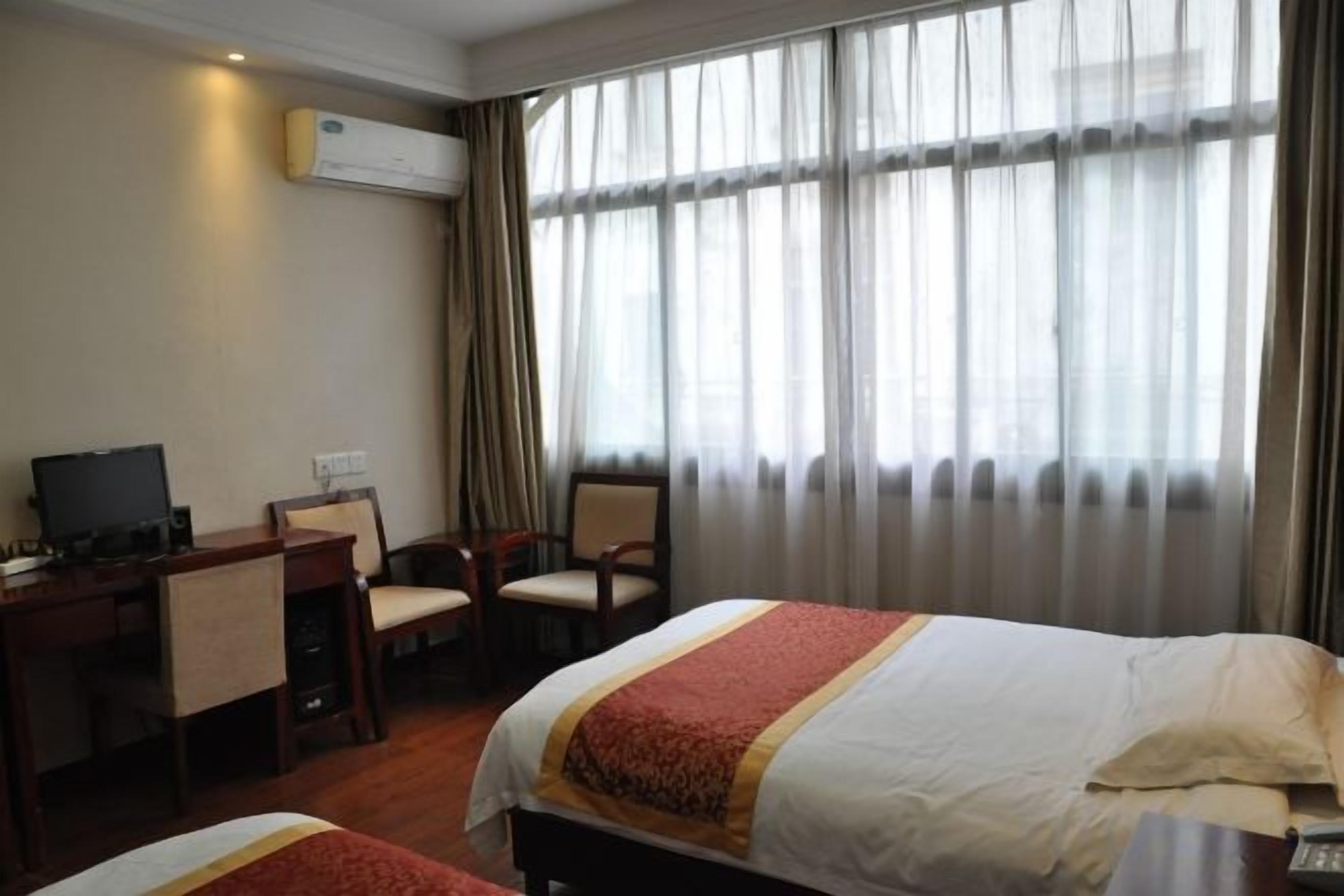 A hotel room with a bed, a desk with a chair, a television, and a window with curtains.