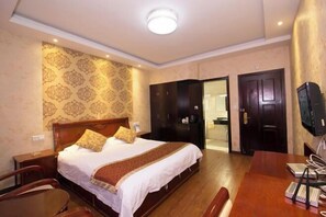 Quarto de hotel com cama, escrivaninha, cadeira, guarda-roupa e televisão.