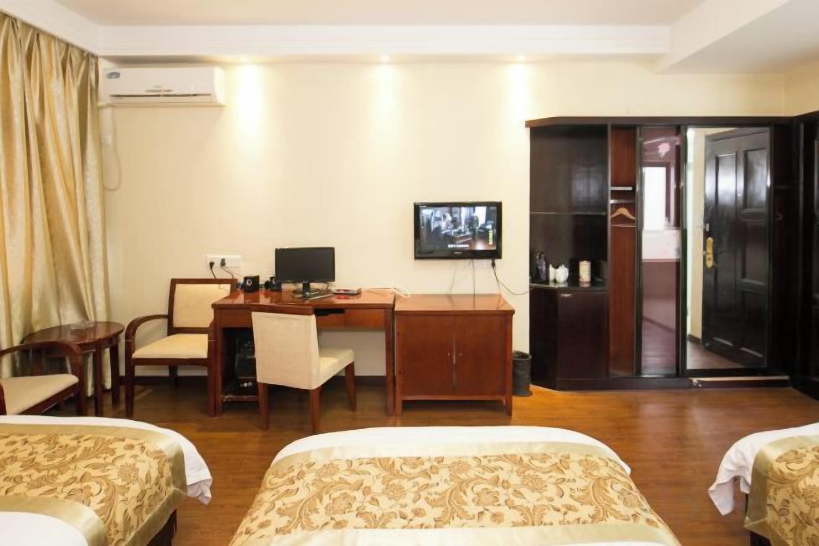 Una habitación de hotel con dos camas, un escritorio con computadora, televisor y armario.