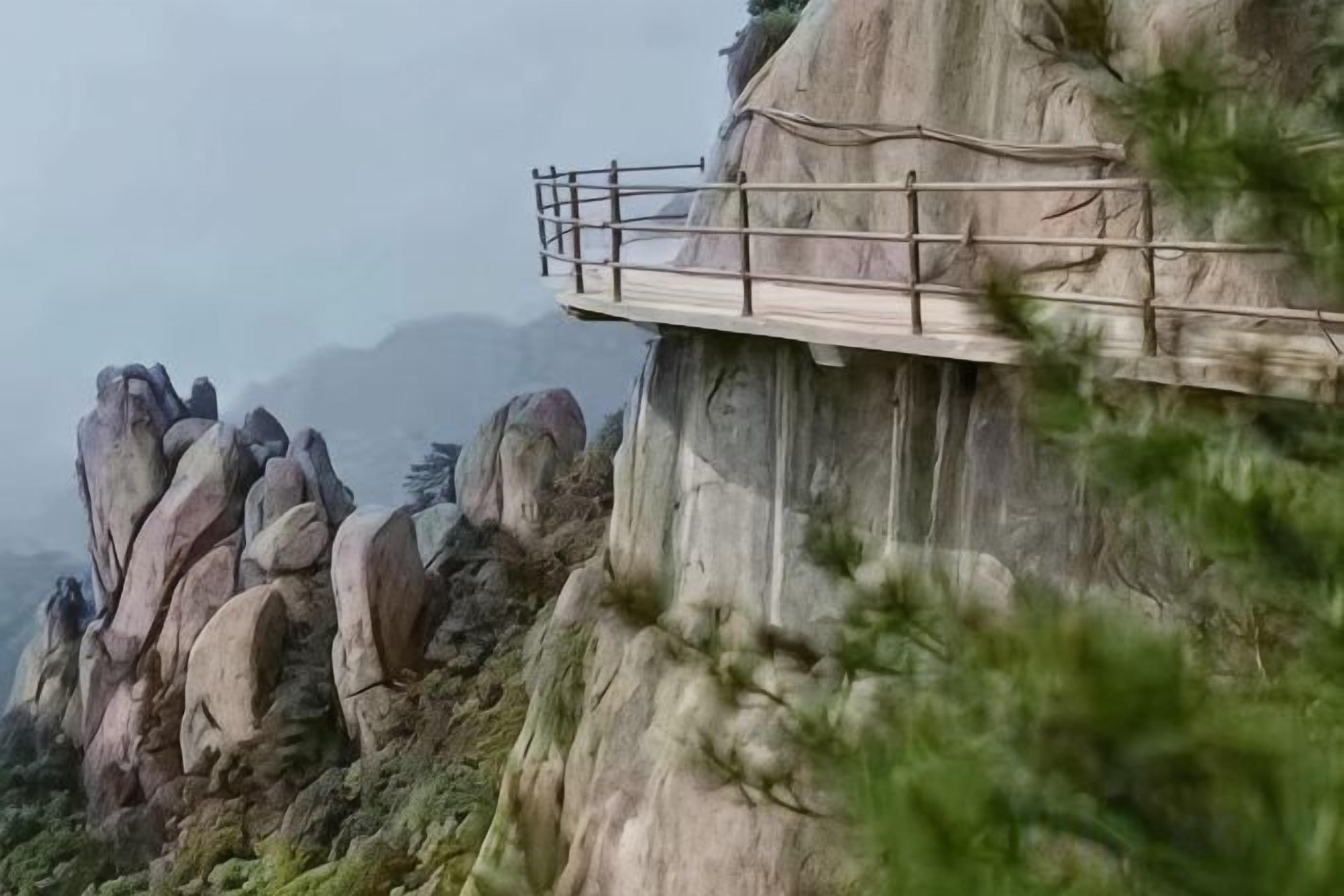 A narrow wooden walkway on a cliffside with a railing, overlooking a rocky landscape.