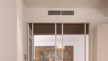 Ein modernes Wohnzimmer mit einer Couch, einem Esstisch mit Stühlen, einem großen Fenster mit Jalousien und einem dekorativen Bild an der Wand.