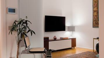 Ein modernes Wohnzimmer mit Flachbildfernseher, einer Zimmerpflanze, einem Sessel, einem Beistelltisch und einem runden Couchtisch.