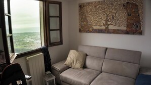 A room with a view through a window, a beige sofa, a radiator, and a patterned artwork on the wall. - Nice rustico with see view (Canal D'oro)