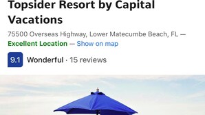 A beach view with a blue umbrella and striped lounge chairs.