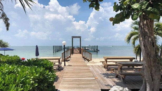 A wooden boardwalk leading to a beach with benches and a lamp post.