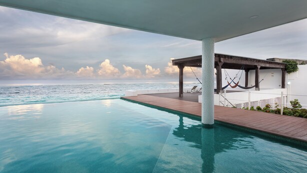 An infinity pool with a wooden deck and a hammock, overlooking the ocean. - Villa de Lujo en Primera Línea de Playa (San Luis)