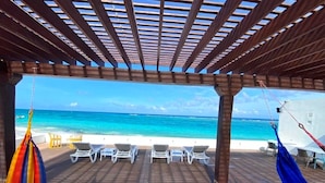 A covered outdoor area with a wooden deck, lounge chairs, and a view of the ocean. - Villa de Lujo en Primera Línea de Playa (San Luis)