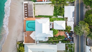 An aerial view of a coastal property with a swimming pool, multiple buildings, and a road adjacent to the beach. - Villa de Lujo en Primera Línea de Playa (San Luis)