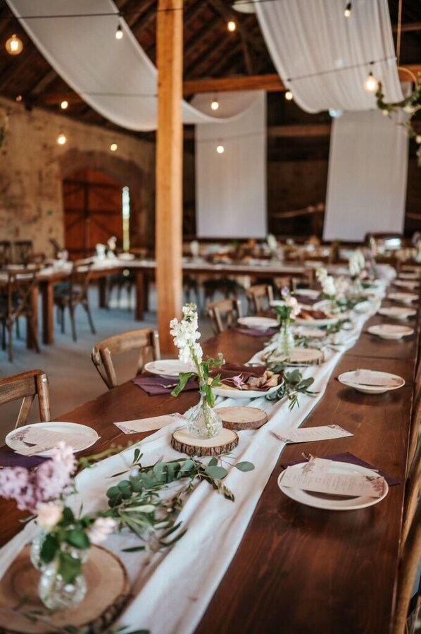 A long dining table set with white tablecloths, wooden centerpieces, and floral arrangements.