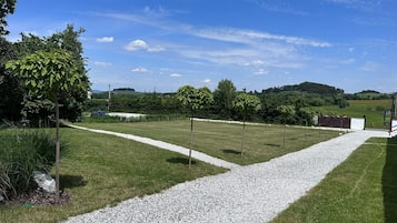 A grassy area with a gravel path, trees, and a distant view of hills.