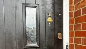 Una puerta negra con un aldabón de latón, un panel de vidrio y un buzón.