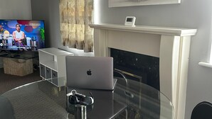 Una sala de estar moderna con una mesa de vidrio, una chimenea, un televisor y un cuadro en la pared.