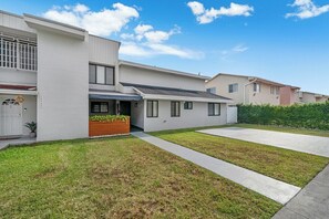 A modern two-story house with a flat roof, a front porch with a wooden bench, and a well-maintained lawn. - Westchester Garden Su (Miami)